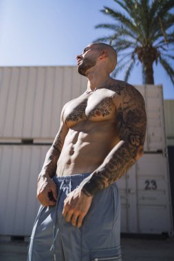 Güneşli bir günde duvarın yanında şortsuz bir adam duruyor.