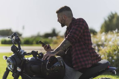 Sakallı yakışıklı adam parkta elektrikli bir motosikletin üzerinde oturuyor.