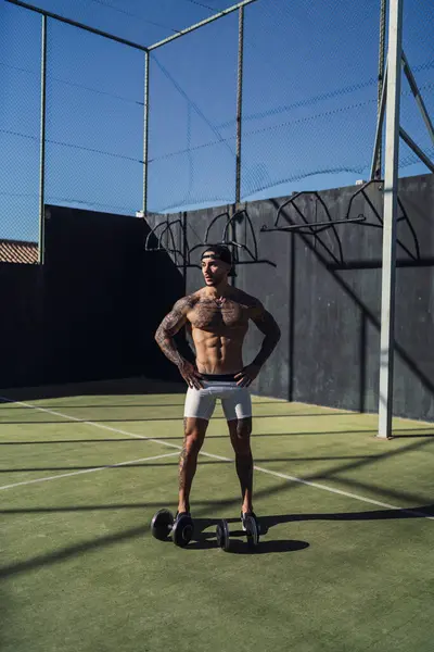 Yakışıklı genç adam dışarıda halterlerle egzersiz yapıyor.