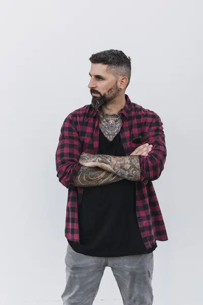Dövmeli genç adam beyaz arka planda poz veriyor.