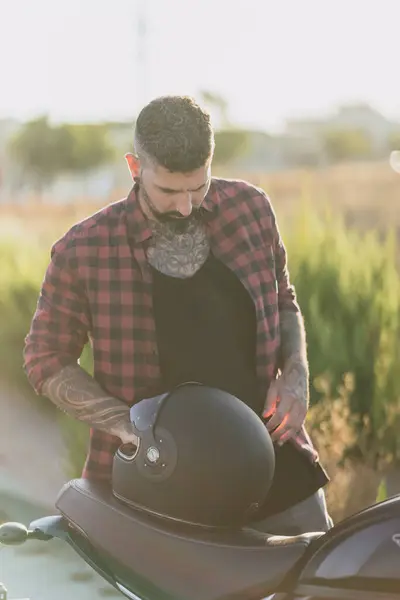 Elinde motosikletle duran bir adam.