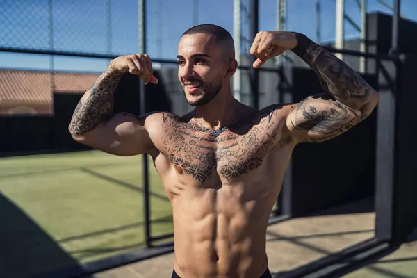 Dövmeleri dışarıda poz veren yakışıklı, kaslı bir adam.