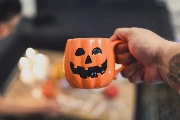 Yaklaştın. Cadılar Bayramı kostümü giymiş bir adam elinde kahve ve balkabağı tutuyor.