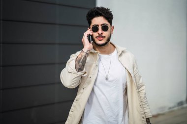 Güneş gözlüklü, şık giyinmiş, telefonda konuşan ve ellerini telefonda tutan yakışıklı bir hippi..