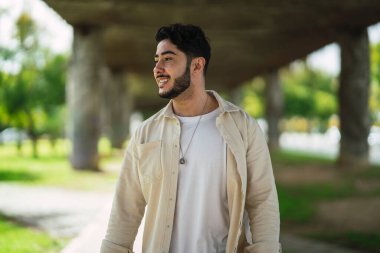 Beyaz gömlek ve siyah pantolon giyen yakışıklı sakallı genç adamın portresi.