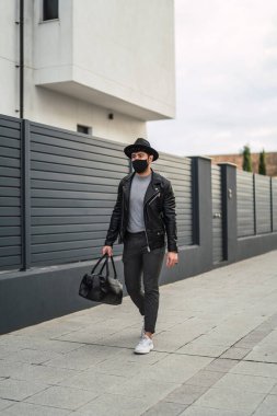Güneş gözlüklü ve siyah şapkalı yakışıklı adam şehirde yürüyor..