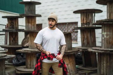 Şapkalı ve gömlekli genç adam sokakta poz veriyor.