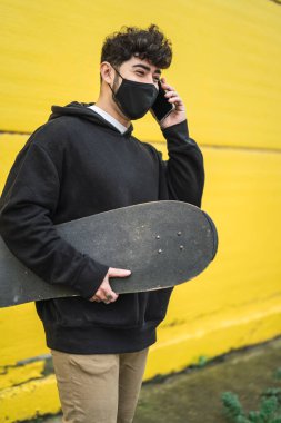 Maskeli genç adam telefonda konuşuyor.