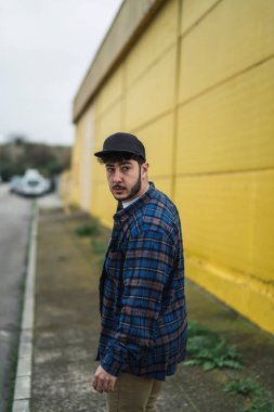 Siyah ceketli ve arka planda sırt çantası olan şapkalı bir adam.