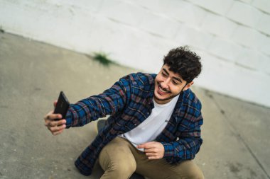 Genç adam günlük kıyafetlerle akıllı telefondan selfie çekiyor.