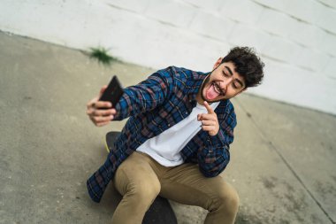 Mutlu genç adam akıllı telefondan selfie çekiyor.