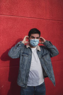 Adam koruyucu maske takıyor ve kameraya bakıyor..