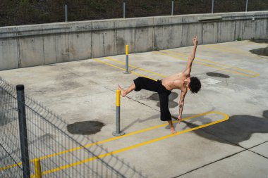 Genç adam bir direğin üzerinde egzersiz yapıyor.