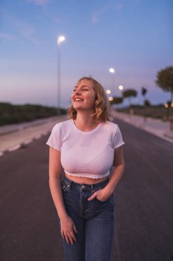 Kot ceketli gülümseyen kız günbatımında poz veriyor..