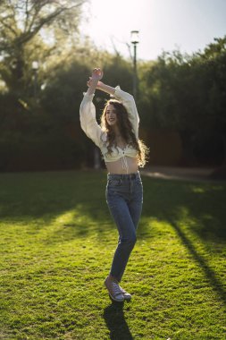 Genç kadın kulaklıkla müzik dinliyor ve parkta dans ediyor.