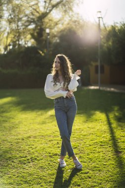 Beyaz kazaklı genç bir kadın parkta yürüyor..