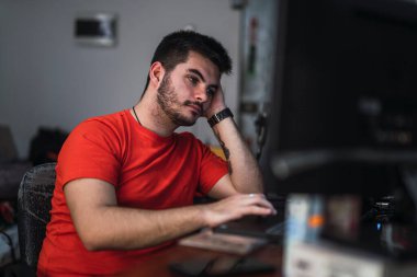 Genç bir adam geceleri ofiste dizüstü bilgisayarla çalışıyor.