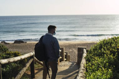 Gün batımında kumsalda yürüyen bir adam sırt çantasıyla