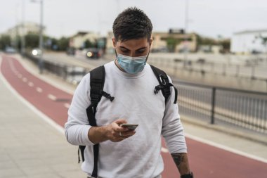 Tıp maskeli genç adam sokakta akıllı telefon kullanıyor..