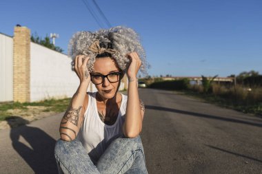 Beyaz kazaklı, mavi gözlüklü yeşil çimenli ve ahşap çitli güzel bir kadın. Arka planda gözlüklü kız.