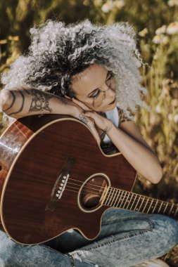 Çimlerde gitar çalan genç bir kadın.