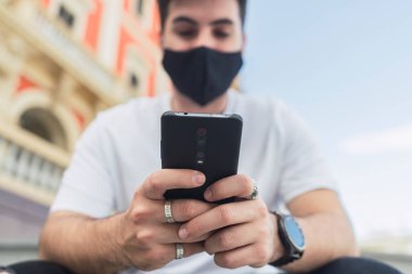 Şehirde akıllı telefon kullanan yüz maskeli bir adamın portresi, covid - 19