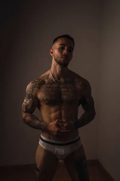 Stüdyoda poz veren kaslı vücutlu genç bir adam.