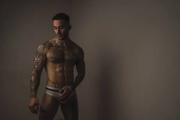 Gövdesi dövmeli, iç çamaşırlı ve dövmeli kaslı bir adam.