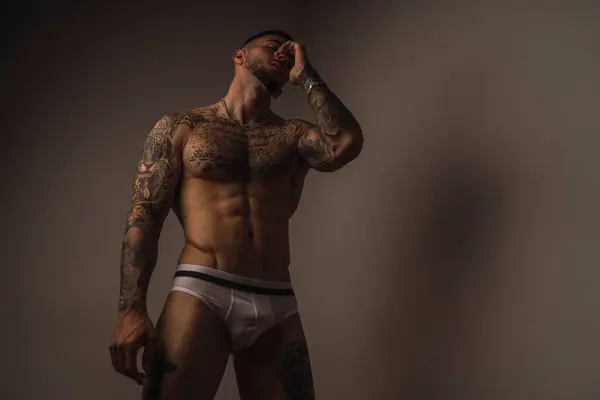 Dövmeleri olan yakışıklı, kaslı, üstsüz bir adam.