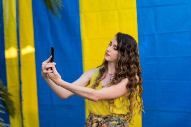 Sarı elbiseli genç bir kız ellerinde selfie ile Ukrayna ulusal gününde sarı bir arka planda.