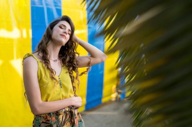 Sarı saçlı, mavi gözlü, sarı elbiseli ve kot pantolonlu güzel bir kızın portresi..