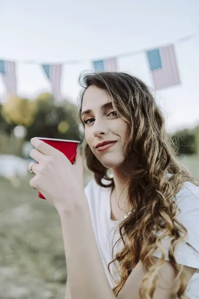 Beyaz gömlekli ve kot pantolonlu kadın bira içiyor.