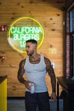 Dövmeleri ve dövmeleri olan genç bir adam spor salonunda duruyor.