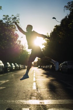 Genç sporcu güneş doğarken bir şehir parkında atlayıp koşuyor.