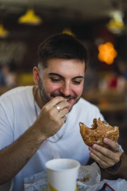Genç yakışıklı beyaz adam hızlı bir kafede lezzetli sandviçleri yemekten zevk alıyor.