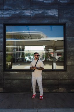 Modern şehirde duran güneş gözlüklü şık genç adam.