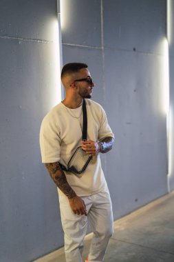 Beyaz duvarın yanında duran dövmeli şık bir adamın portresi