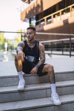 Parkta yerde oturan genç bir adamın portresi. Genç yakışıklı adam parkta antrenmandan sonra dinleniyor..