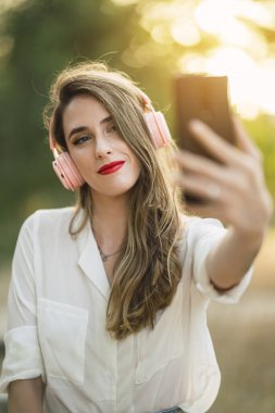 Kulaklıklı genç bir kadın selfie çekiyor.