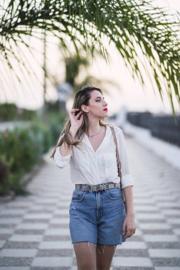 Uzun dalgalı saçlı, beyaz gömlekli ve kot pantolonlu güzel bir kadın.