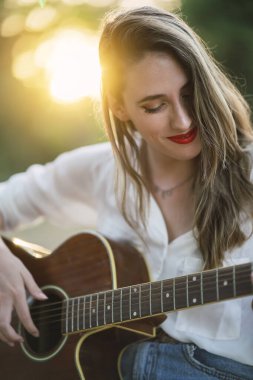 Parkta gitar çalan genç bir kadın.