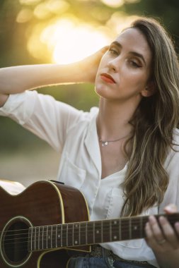 Gün batımında dışarıda gitar çalan genç bir kız.