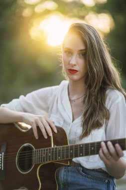 Parkta gün batımında gitar çalan güzel bir kız.