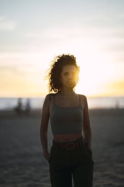 Gün batımında poz veren kıvırcık saçlı genç bir kadın.