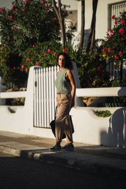 Sokakta beyaz çiçeklerle yürüyen, günlük giysiler ve siyah elbiseler içinde genç bir kadının portresi.