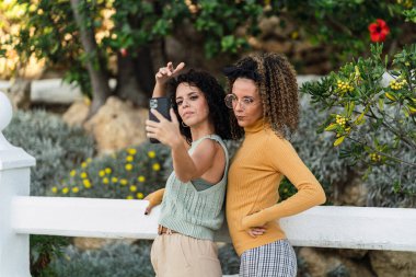 Şehir parkında kameralı ve cep telefonlu iki güzel kadın.