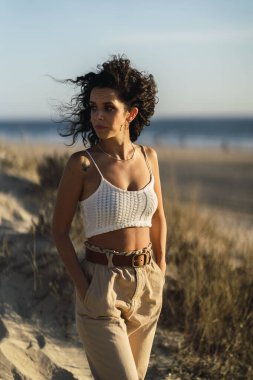 Genç bir kadın kumsalda beyaz kum tepelerinde poz veriyor.