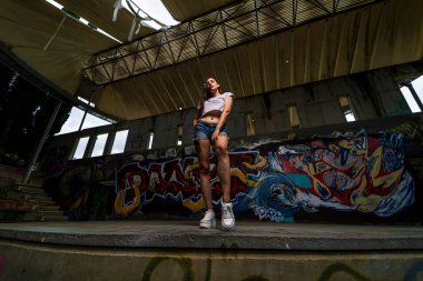 Kız köprüde poz veriyor, siyah şort ve spor ayakkabı giyiyor, kameraya poz veriyor..