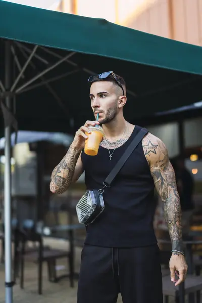 Genç adam su içiyor ve şişeyi sokakta tutuyor.