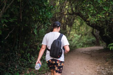 Sırt çantalı siyah ceketli bir adam ormanda yürüyor..